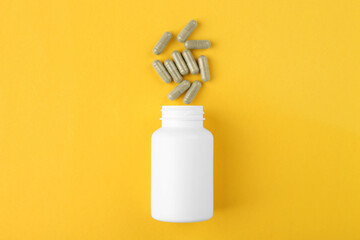 Bottle and vitamin capsules on yellow background, top view