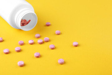 Bottle and vitamin pills on yellow background, closeup. Space for text