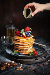 Pile of pancakes with blueberries and strawberries on a plate with dark background  