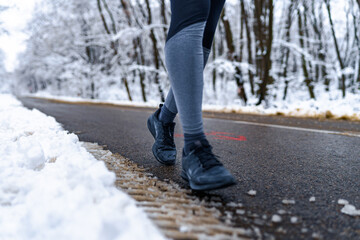 Closeup image of a person walking on wet road, snow on the ground and sports equipment in focus.
