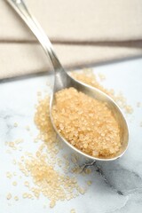 Spoon with brown sugar on white marble table, closeup
