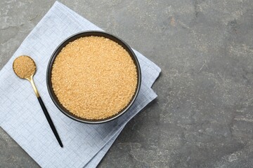 Brown sugar in bowl and spoon on grey textured table, top view. Space for text