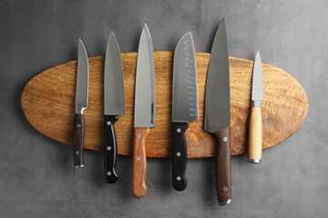 Many different knives and wooden board on grey textured table, flat lay