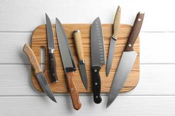 Many different knives and board on white wooden table, flat lay