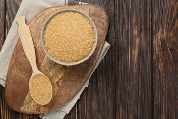 Brown sugar in bowl and spoon on wooden table, flat lay. Space for text