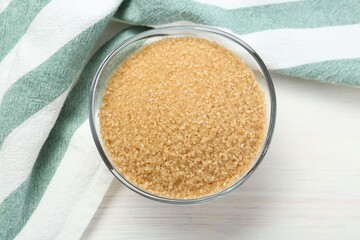 Brown sugar in glass bowl on white wooden table, top view