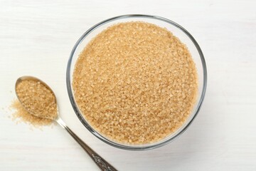 Brown sugar in bowl and spoon on white wooden table, flat lay