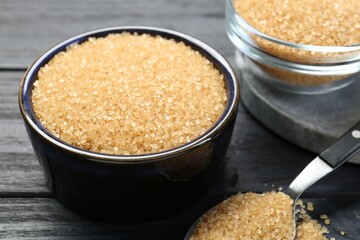 Brown sugar in bowls and spoon on black wooden table, closeup