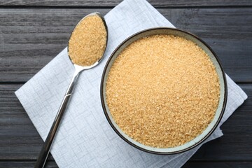 Brown sugar in bowl and spoon on black wooden table, flat lay