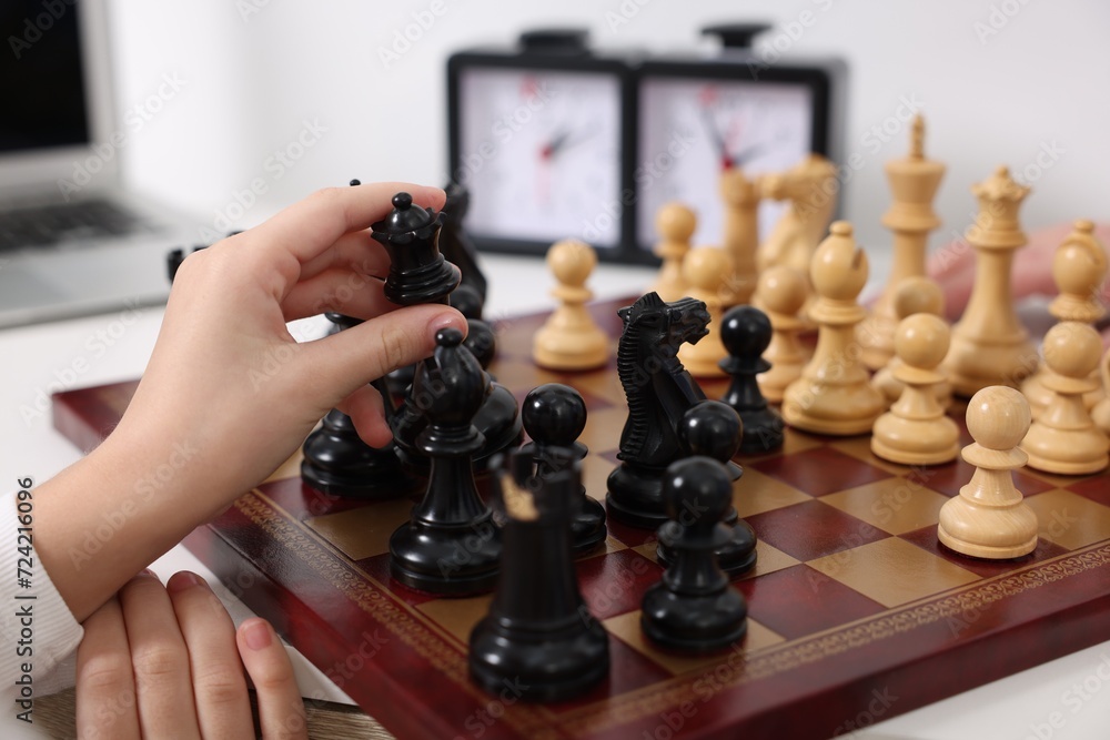 Wall mural Little child playing chess at table indoors, closeup