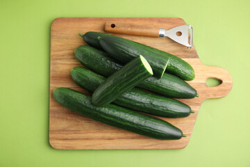 Fresh cucumbers and peeler on green background, top view