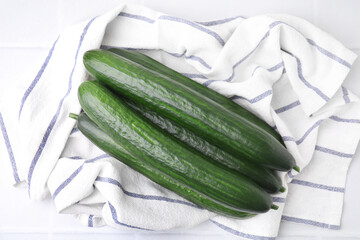 Fresh cucumbers and cloth on white table, top view