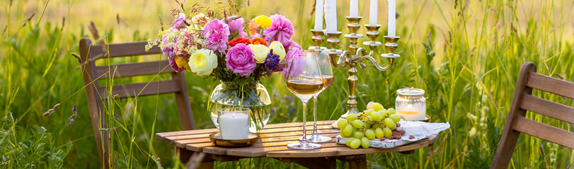 Elegant wedding or private party for a loving couple table setting outdoors in the garden. Beautiful decor with fresh ranunculi flowers, candles. Gourmet cheese board, fruits, white wine. Banner