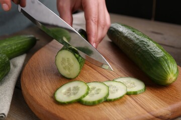 Woman cutting cucumber on wooden board at table, closeup