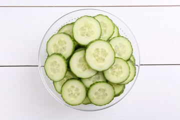 Cut cucumber in bowl on white wooden table, top view