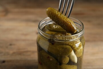 Eating tasty pickled cucumber from jar at table, closeup