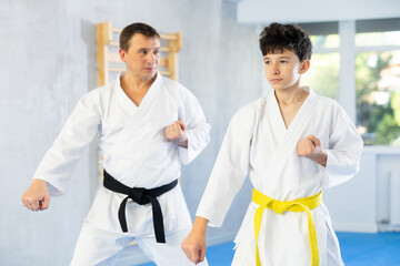 Adult man and boy teenager in kimono practice karate technique in gym