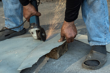 Worker using a electric grinder to cut a Zinc steel while sparks are flying.