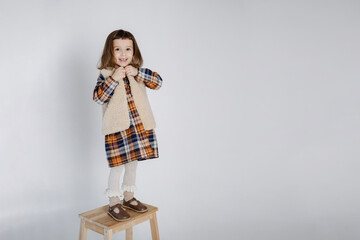 studio portrait of a beautiful girl wearing a checkered dress and a woolen vest