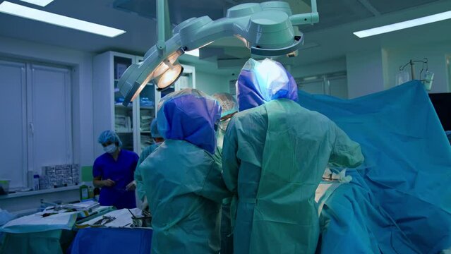 Medical team work at the operational table. Male assistant prepares tools for the doctors.