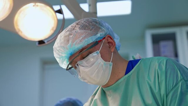 Male doctor in mask, cap and protective glasses. Close up portrait of a surgeon at work.