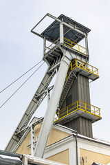 A mine hoist shaft against a gray sky. Close up of the wheels at the top of the shaft.