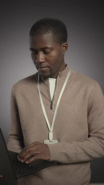 Vertical medium studio portrait of young Black male software engineer posing for camera with laptop on grey background