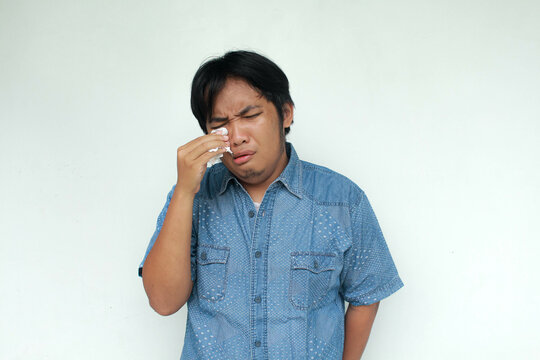 Crying face of Asian man with hand holding tissue isolated on gray background.