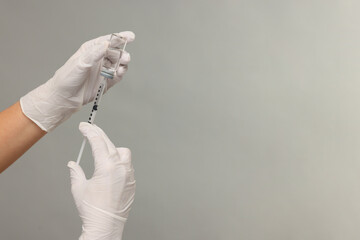 Doctor filling syringe with medication from glass vial on grey background, closeup. Space for text