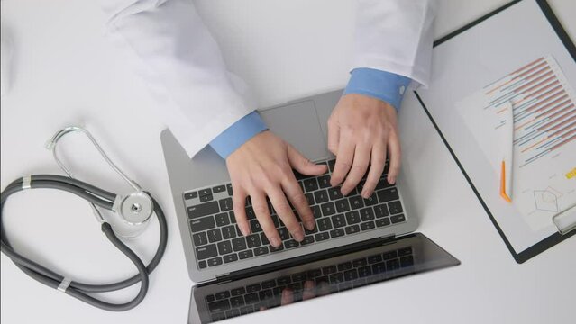 A specialist in the field medicine works with electronic prescriptions and documents. A doctor concentrates on working at desk, using technology, working on laptop. Hands typing on keyboard top view