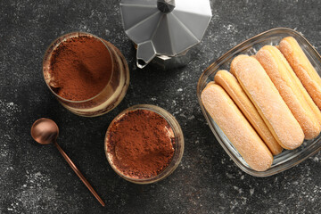 Delicious tiramisu in glasses and ingredients on grey textured table, flat lay