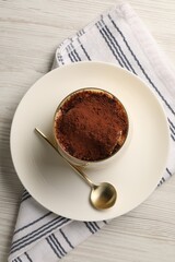 Delicious tiramisu in glass and spoon on white wooden table, top view
