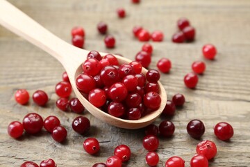 Spoon with fresh ripe cranberries on wooden table, closeup
