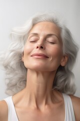 A gorgeous happy smiling senior woman with closed eyes and long grey hair over a grey background