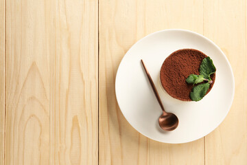 Tasty tiramisu and mint in glass on light wooden table, top view. Space for text