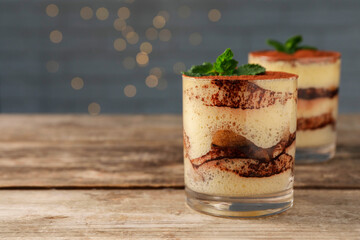 Tasty tiramisu and mint in glasses on wooden table, closeup. Space for text