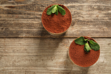 Tasty tiramisu and mint in glasses on wooden table, top view. Space for text