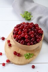 Fresh ripe cranberries in bowl and branches on white wooden table