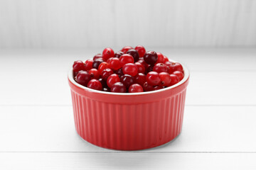 Fresh ripe cranberries in bowl on white wooden table, closeup
