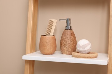 Different bath accessories and personal care products on shelving unit near beige wall