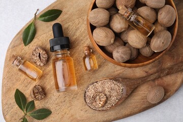 Fototapeta na wymiar Nutmeg essential oil, nuts and leaves on light table, top view
