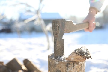 Man taking axe out of wooden log outdoors on winter day, closeup. Space for text