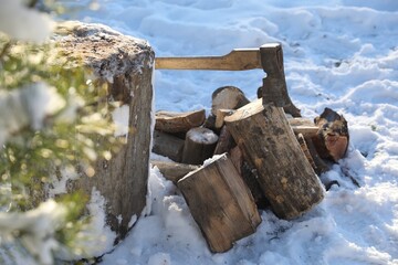 Metal axe in wooden log and pile of wood outdoors on sunny winter day