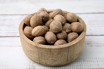 Whole nutmegs in bowl on light wooden table, closeup