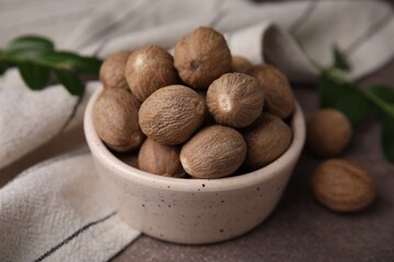 Whole nutmegs in bowl on brown table, closeup