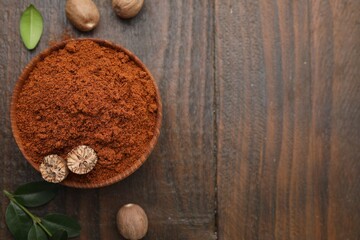 Nutmeg powder in bowl, seeds and green leaves on wooden table, flat lay. Space for text