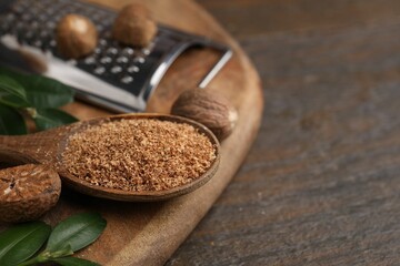 Spoon with grated nutmeg and green leaves on wooden table, closeup. Space for text