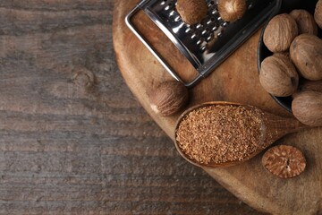 Spoon with grated nutmeg, seeds and grater on wooden table, top view. Space for text