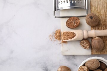 Scoop with grated nutmeg, seeds and grater on white marble table, flat lay. Space for text