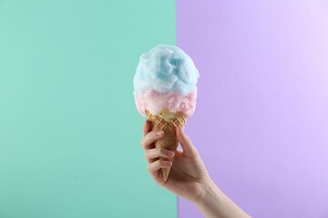 Woman holding waffle cone with cotton candy on color background, closeup